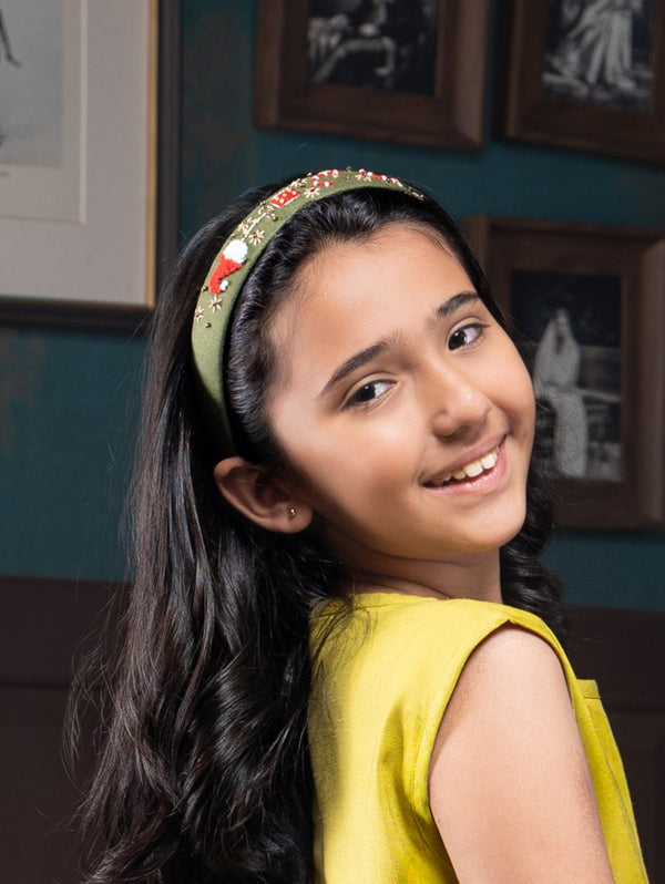 Young girl in a yellow dress with a decorative headband, smiling in a room with framed pictures on the wall.